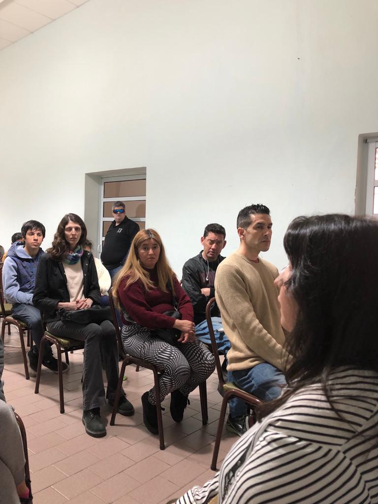 Se ven algunas personas con discapacidad visual que asistieron al taller de orientación laboral en MUCAR, en la ciudad de Rosario. Son 4 varones y dos mujeres sentados en sillas escuchando atentamente a Florencia, del Programa Ágora.